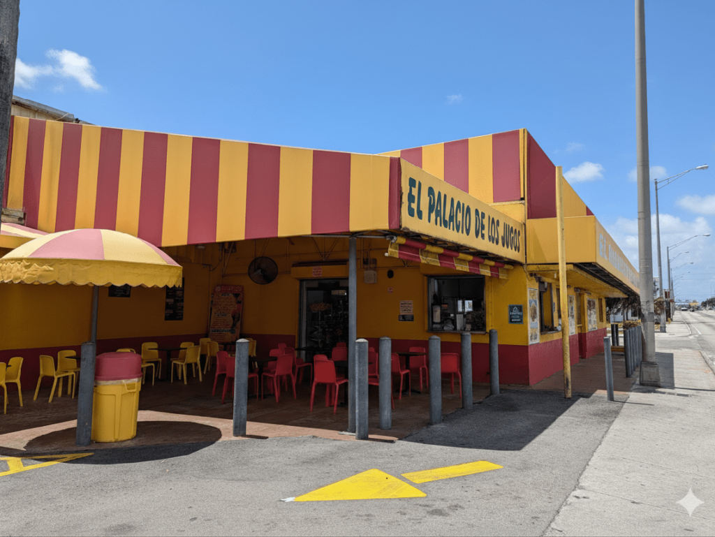 Side view of El Palacio de los Jugos at NW 20th St & NW 27th Ave: Large red and yellow awning, red and yellow tables.