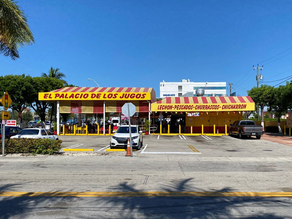 El Palacio de los Jugos Coral Way front view with red and yellow awnings and outdoor parking. 
